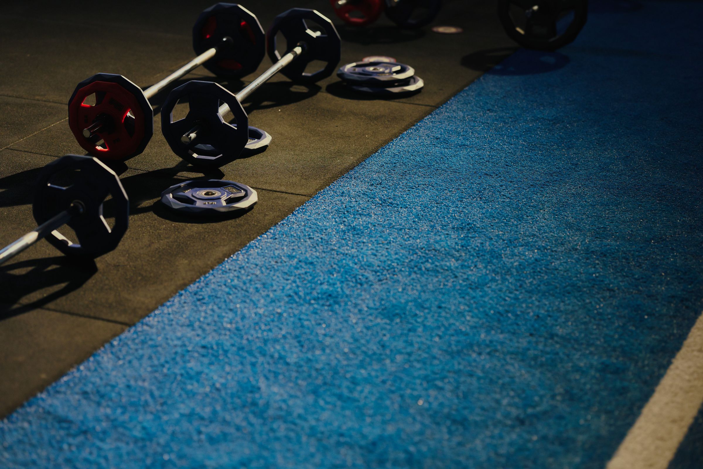 Barbells and plates resting beside the blue turf in an Apex F45 studio